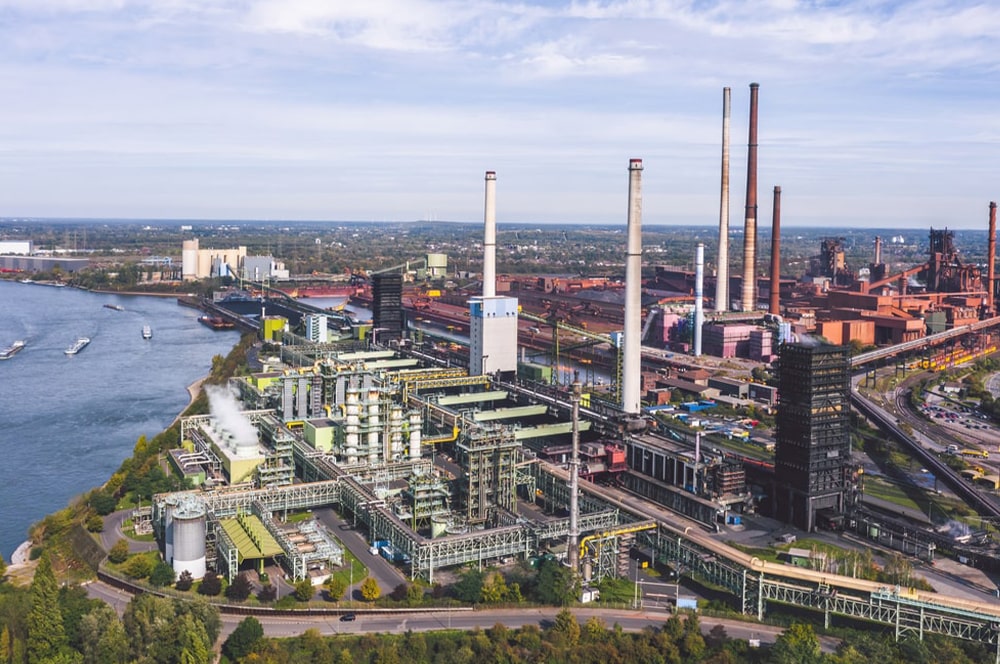 Thyssenkrupp-stahlwerk-szene-transformationsgipfel-aufruf Duisburg mit Schornsteinen am Fluss.