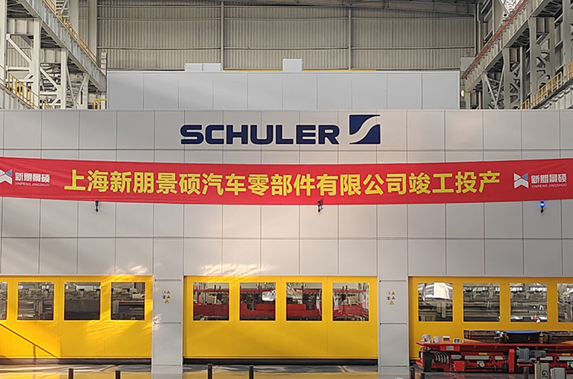 Das Bild zeigt eine Werkshalle des chinesischen Unternehmens Xin Peng. An einer Wand hängt ein rotes banner mit chinesischen Schriftzeichen, darunter sind drei gelbe Maschinen zu sehen.