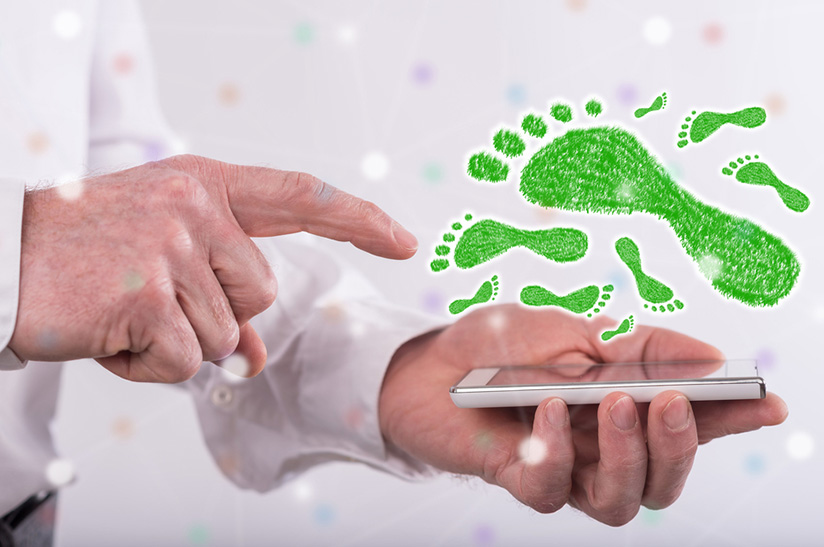 Der Stahlhändler Klöckner bietet individualisierte CO2-Fußabdrücke an. Das Bild zeigt das symbolisch: mit einer linken Hand, in der ein Smartphone liegt, über dem grüne Fußabdrücke unterschiedlicher Größen zu sehen sind. Der ausgestreckte Zeigefinger der rechten Hand will das Smartphone berühren.