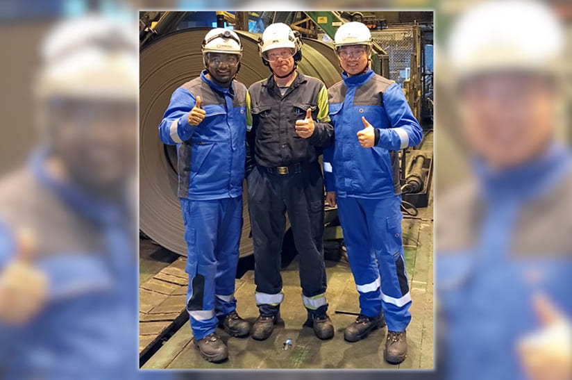 Das Bild zeigt drei Männer im Blaumann: Premsingh Bist, Projektleiter und leitender Ingenieur bei Primetals Technologies, Jari Puurtinen, Entwicklungsleiter für Prozessautomatisierung und Projektleiter für Elektrik und Automatisierung bei SSAB Hämeenlinna, und Dong Yan, Ingenieur für die Inbetriebnahme von Antrieben bei Primetals Technologies, vor Ort, als das erste Coil, nach Abschluss von Phase 1 der Modernisierung des Walzgerüsts bei SSAB Hämeenlinna, produziert wurde.