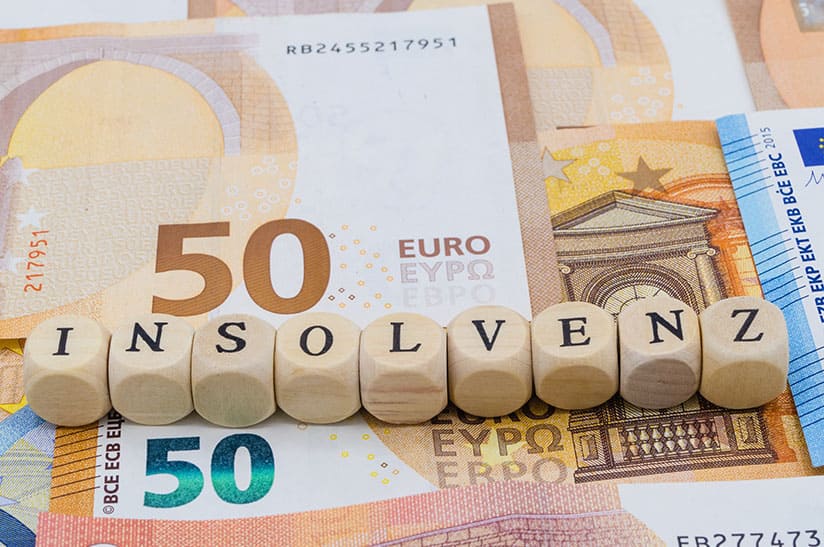 Das Bild zeigt neun Würfel, die nebeneinander liegen und das Wort Insolvenz bilden. Unter den Würfeln liegen Geldscheine. In dem dazugehörigen Artikel geht es um die Insolvenzantragspflicht.