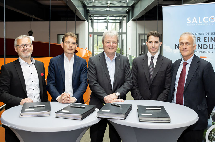 Das Bild zeigt fünf weiße Männer in Business-Outfits, die hinter Stehtischen stehen. Einer von ihnen gehört zur Salzgitter AG.