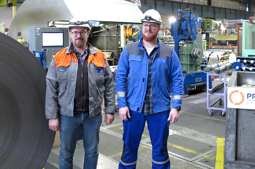 Das Bild zeigt zwei Arbeiter in Kluft im stahlwerk-szene-transformationsgipfel-aufruf von thyssenkrupp Rasselstein in Andernach, Deutschland. Dort hat Primetals Technologies eine modernisierte Band-Längsteilanlage in Betrieb gesetzt.