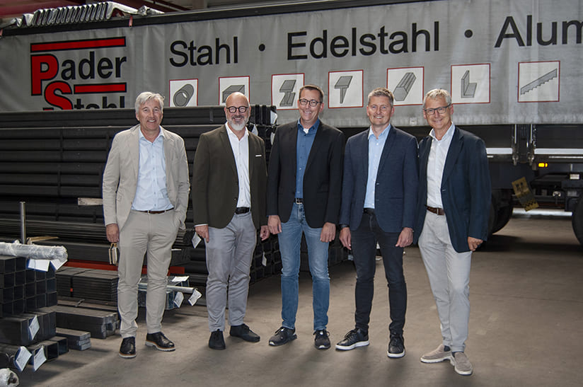 Fünf Männer stehen in einer Lagerhalle, Im Hintergrund ist ein LKW mit dem Schriftzug Pader-Stahl.