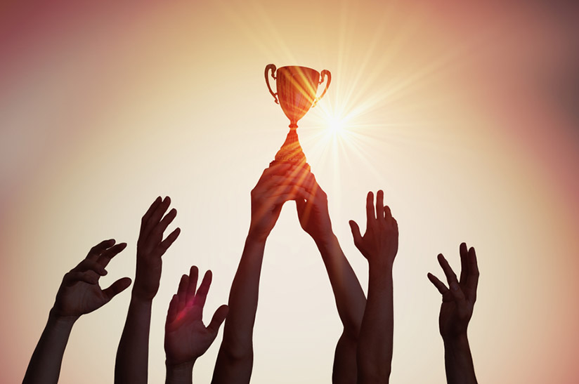 Das bild zeigt im Gegenlicht sieben in die Höhe gereckte Unterarme. Ein paar Hände hält dabei einen Pokal fest. Das Bild steht sinnbildlich für die jüngste Auszeichnung von Dillinger.