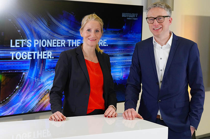 Das Bild zeigt eine weiße Frau (Birgit Held) und einen weißen Mann (Stephan Knüttel), die an einem Stehtisch stehen. Sie tragen Business-Kleidung und gehören zum Unternehmen Benteler.
