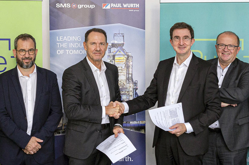 Das Bild zeigt vier weiße Männer im Sakko, die beiden ind er Mitte schütteln sich die Hände und halten jeweils einen Vertrag in der Hand. Es handelt sich um Personen von den Unternehmen SMS digital, Paul Wurth und Dillinger / saarstahl-werk-voelklingen-uebernahme-liberty-ascoval-hayang, die den Hochofenbetrieb optimieren wollen.