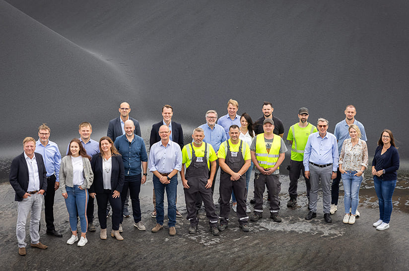 Das Bild zeigt eine Gruppe von 21 Menschen in Büro- und Arbeitskleidung. Es handelt sich um Mitarbeiter von Cremer Erzkontor und HAG.