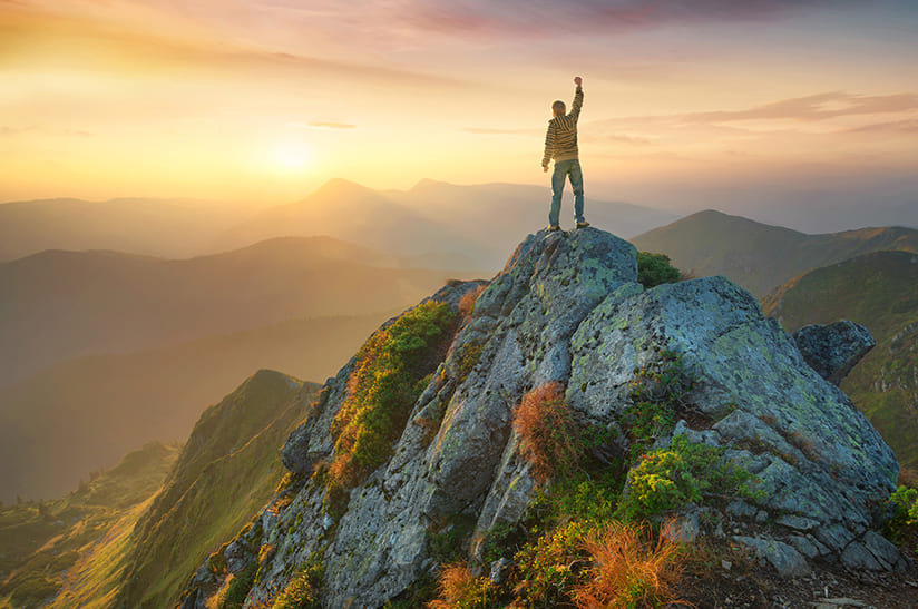 Das Bild zeigt einen Tourist auf dem Gipfel eines hohen Felsens. Der Tourist reckt den rechten Arm in den Himmel, die hand ist zur Faust geballt. Das Bild steht isnngemäß dafür, dass saarstahl-werk-voelklingen-uebernahme-liberty-ascoval-hayang im Ecovadis-Rating wiederholt die höchste Auszeichnung erhalten hat.