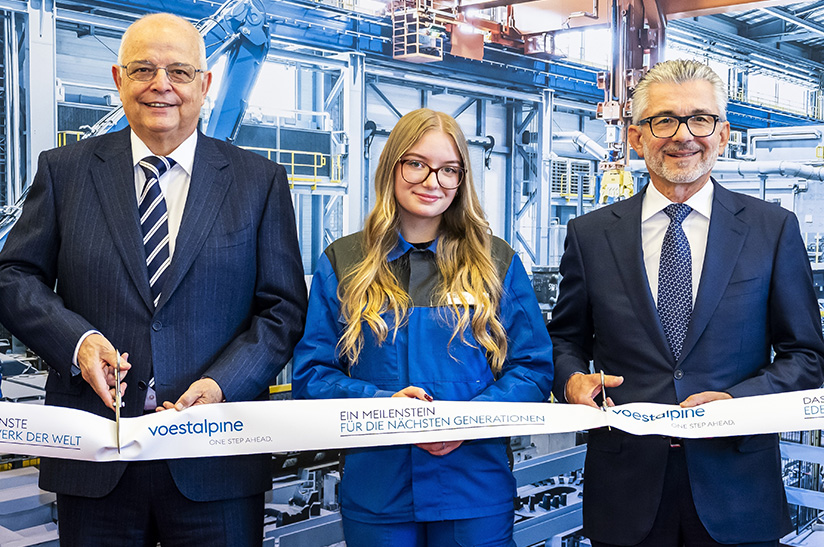 Das Bild zeigt männliche Anzugträger (Führungskräfte) und in ihrer Mitte eine junge Frau im sogenannten Blaumann (Arbeiterin). Alle drei gehören zu Voestalpine und schneiden symbolisch ein Band anlässlich einer Eröffnungsfeier in Kapfenberg durch.