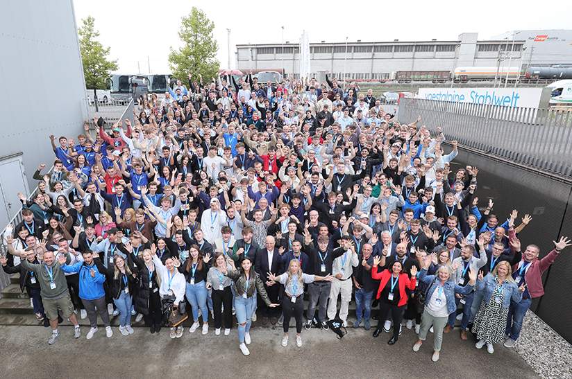 Das Bild zeigt eine große Gruppe junger Menschen, Azubis von Voestalpine im letzten Ausbildungsjahr, die in die Kamera grüßen und lachen.