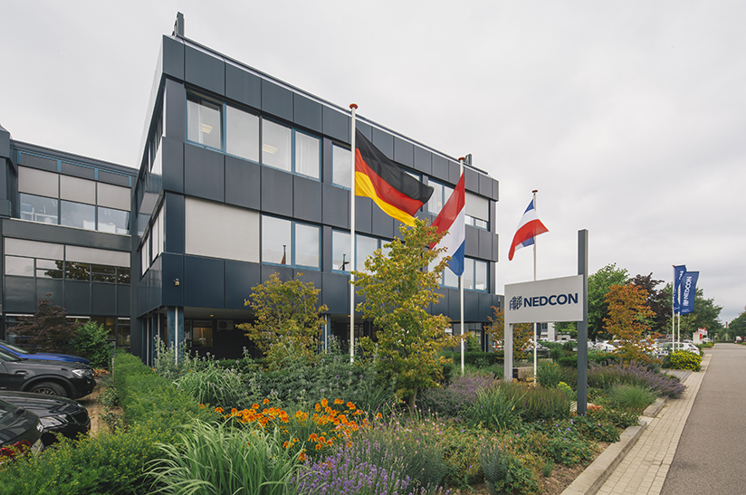 Das Unternehmen zeigt ein Bürogebäude, vor dem Länderflaggen wehen. Es handelt sich dabei um den Sitz von Nedcon, einem Unternehmen von Voestalpine.
