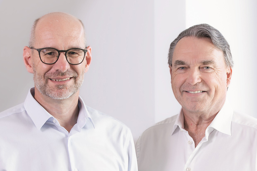 Das Bild zeigt zwei weiße Männer, die helle Hemden tragen und in die Kamera lächeln. Es handelt sich um Dr. Wolfgang Sammer (links, Vorstandssprecher Klüber Lubrication) und Claus Langgartner (rechts, Sammers Vorgänger im Amt).