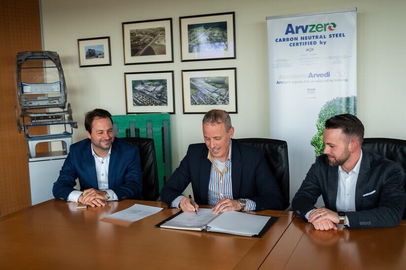 Das Bild zeigt drei Männer an einem Konferenztisch. Der Mann in der Mitte unterzeichnet einen Vertrag. Im Hintergrund ist ein Rollup-Display zum Produkt Arvzero zu sehen.