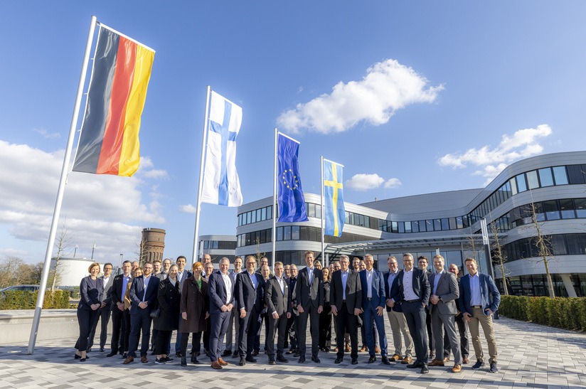 Gruppenfoto vor Bürogebäude mit internationalen Flaggen, Stahlindustrie-Event.