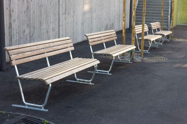 Sitzbänke mit Metallgestell vor Betonwand im Freien, Thema: Stahl und Fachliteratur.