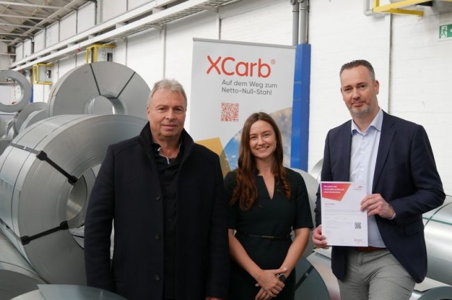 Mitarbeiter in der Stahlfabrik präsentieren XCarb-Zertifikat für Stahlproduktion.