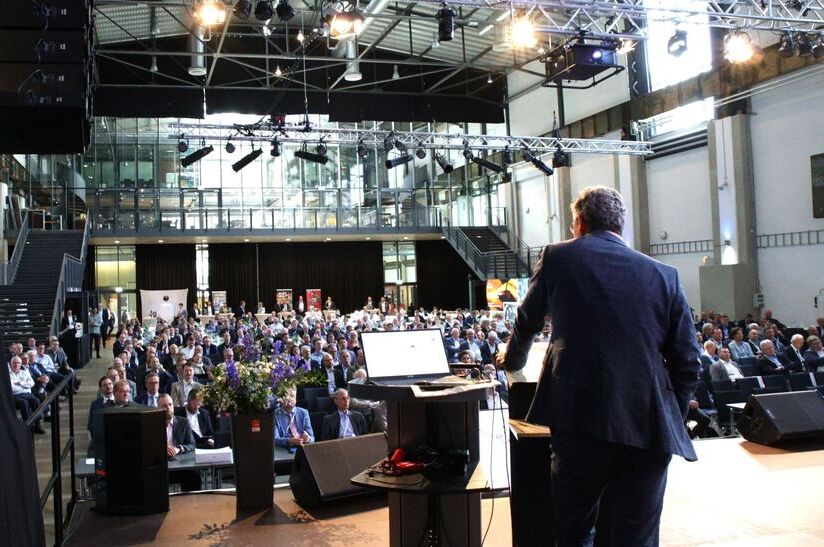 Impression vom VDEh-StahlTag 2025: zu sehen ist der Rücken eines Redners auf der Bühne, der Blick geht in die Halle und zeigt viele Zuhörer