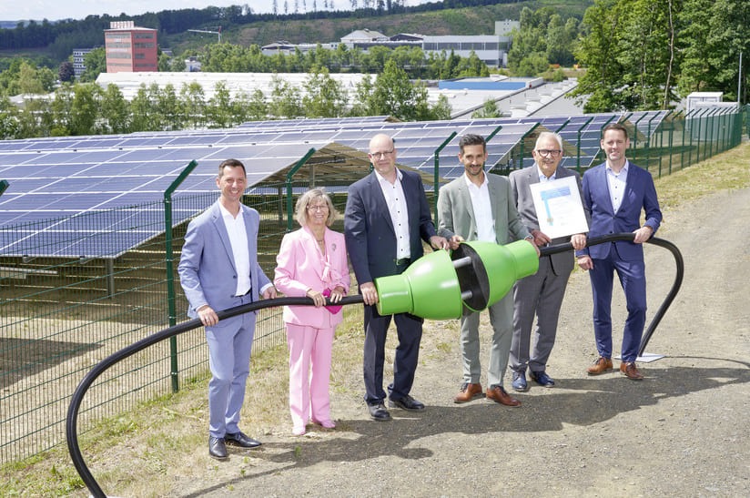 Das Bild zeigt Führungskräfte von Schäfer Werke, die einen überdimensionierten grünen Stromstecker halten. Beim Aufbau der Solaranlage im Hintergrund kam CO2-reduzierter Stahl von ArcelorMittal zum Einsatz.