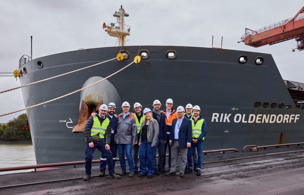 Gruppe von Arbeitern vor Frachtschiff im Stahlbereich, Fachzeitschriften im Verkauf.