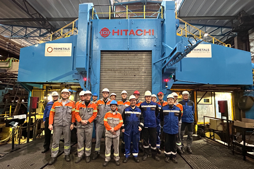 Gruppe von Fachleuten vor einer großen Hitachi-Maschine in einem Stahlwerk.