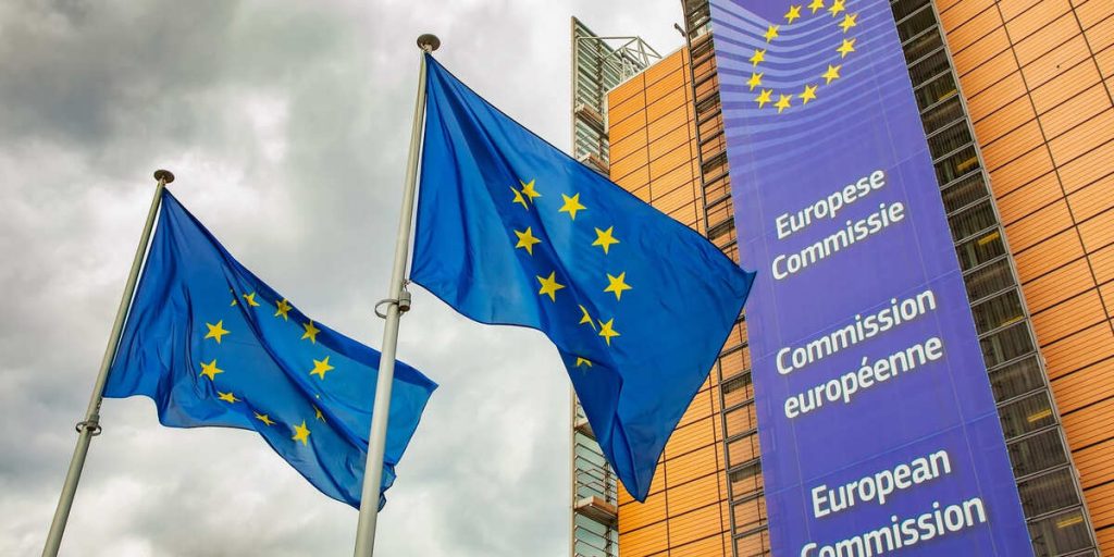 EU-Kommissionsgebäude mit Flaggen. Die EU-Kommission plant ein Automotive Package, um die grüne Leitmärkte zu etablieren.