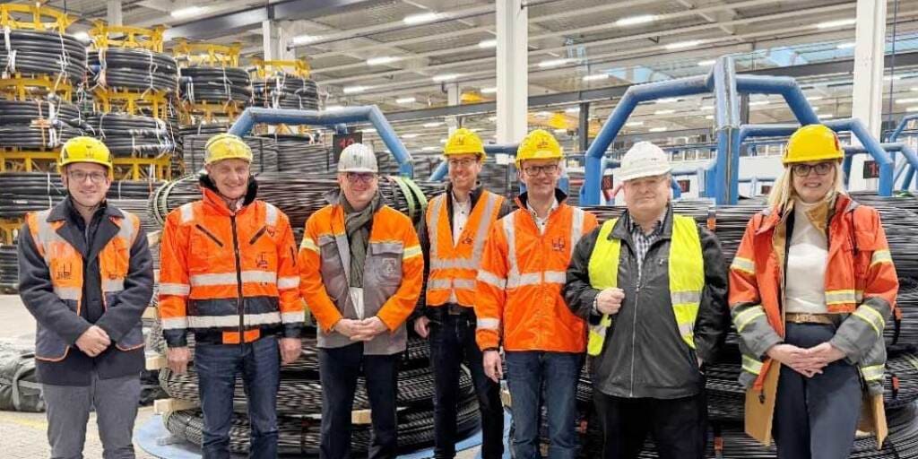 Das Bild zeigt Mitarbeiter in Schutzkleidung in Stahlfabrik, umgeben von großen Stahlrollen. Es geht um Spannstahldraht. und zu sehen sind (v. l.): Sebastian Weizer (Zentralbereichsleiter Komponenten-Produktion, Max Bögl Wind AG), Josef Knitl (Vorstand, Max Bögl Wind AG), Jörg Disteldorf (Personalvorstand der Saarstahl Aktiengesellschaft und verantwortlicher Vorstand für DWK), Tobias Thumann (Leiter Einkauf, Max Bögl Wind AG), Stefan Braun (Kaufmännischer Leiter, Max Bögl Wind AG), Andreas Huf (Geschäftsführer DWK Drahtwerk Köln GmbH), Dr. Nadine Artelt (Sales Director Saarstahl AG)