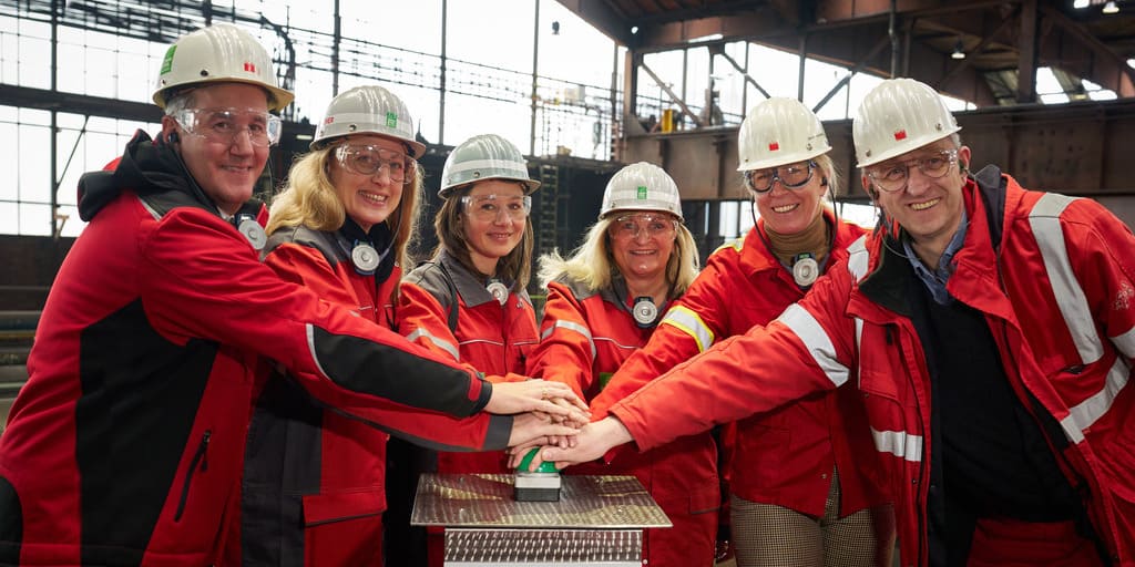 Gruppenfoto von Fachleuten in einer Stahlfabrik mit Schutzhelmen und Arbeitskleidung. Es sind GMH-Führungskräfte anlässlich der Inbetriebnahme der EVA 2.