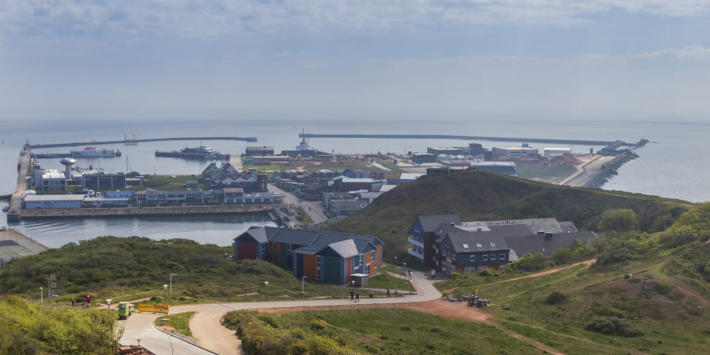 Das Bild zeigt im Vordergrund das Festland der Insel Helgoland und dahinter die Nordsee mit dem Hafen der Insel.