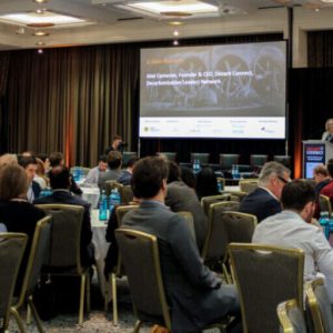 Veranstaltungen 1 Die Decarb Connect Europe 2026 richtet sich an Führungskräfte aus energieintensiven Branchen, die für Anlagen, Energieversorgung oder langfristige Investitionsentscheidungen verantwortlich sind. Das Bild zeigt eine Szene von 2025: Teilnehmer sitzen an Tischen und schauen auf die Bühne, auf der ein Speaker seinen Vorttrag hält.