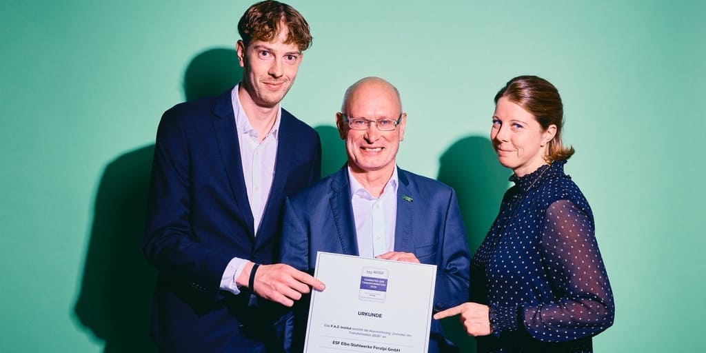 Das Bild zeigt drei Menschen: In der Mitte steht Uwe Reinecke, General Manager von FERALPI STAHL, der eine Urkunde in der Hand hält.